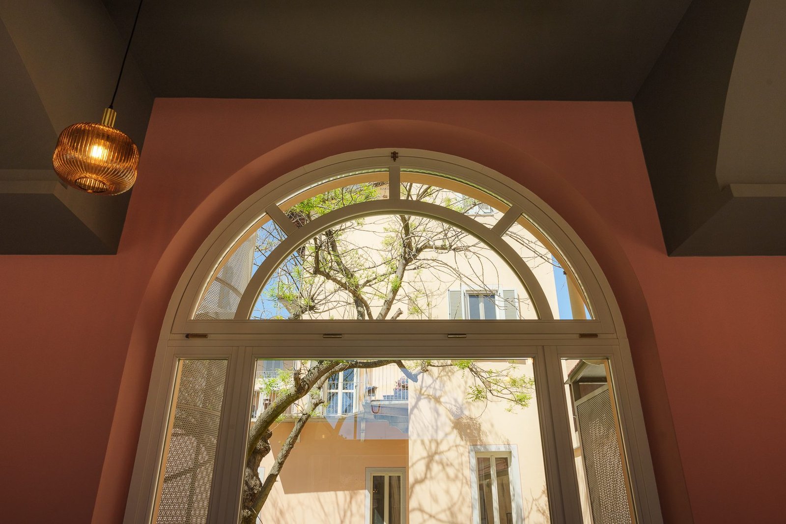 Una finestra ad arco sulla parete color terracotta, con una lampada ambrata